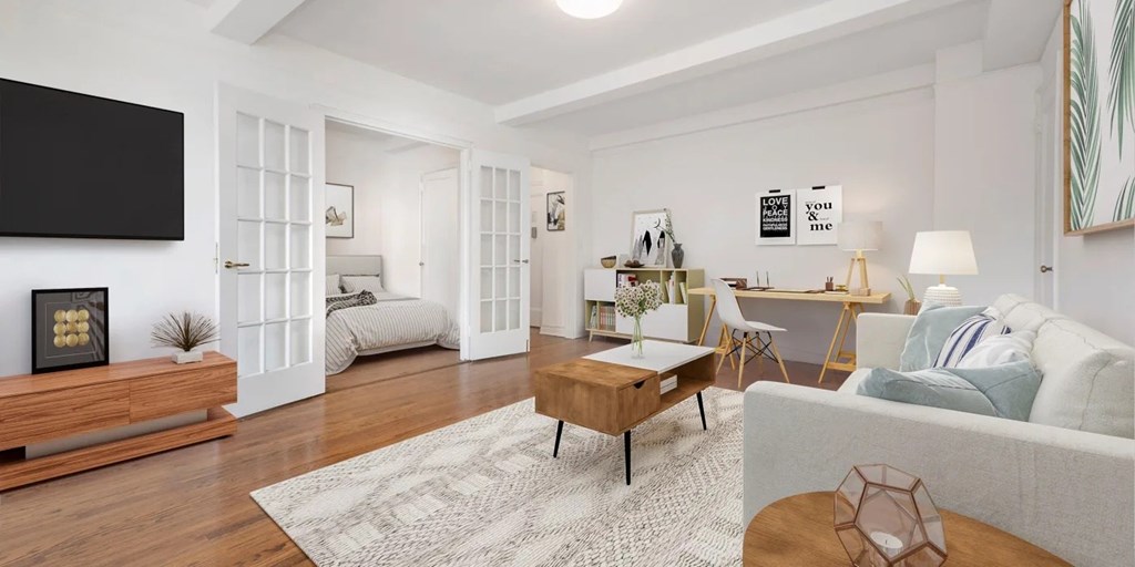 A modern living room with a grey couch, a wooden coffee table, and a flat-screen TV mounted on the wall.at London Terrace Gardens, New York, 10011