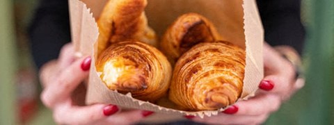 A person holding a paper container filled with croissants.