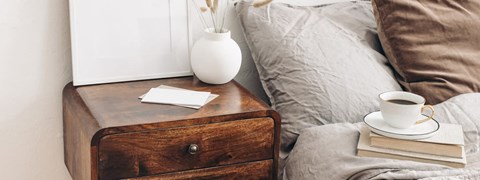 A wooden nightstand with a cup of coffee and a book on top of it.