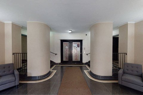 A hallway with a brown carpet and grey couches.