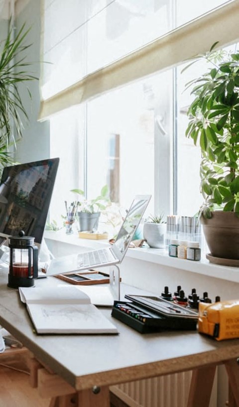 A desk with a laptop, a plant, and a notebook.