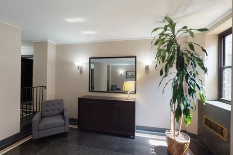 A living room with a grey chair, a mirror, a lamp, and a plant.