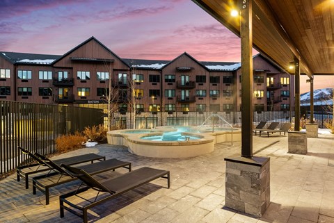 A pool area with sun loungers and a hot tub in front of a building with a mountain in the background.