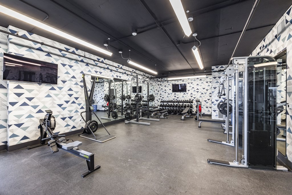a gym with weights machines and a wall with white and blue tiles