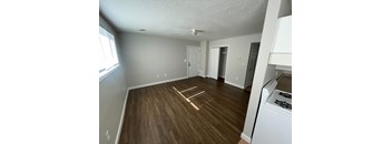 an empty living room with wood flooring and a kitchen