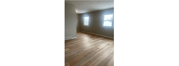 an empty living room with wood flooring and two windows