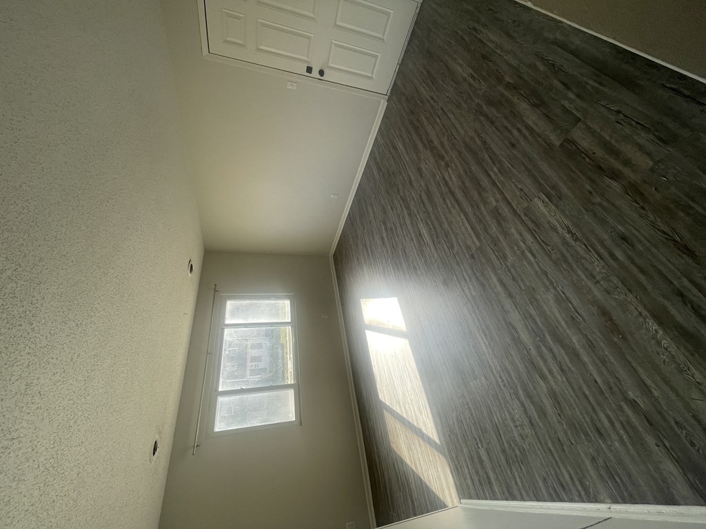 the view from the bottom of a hallway with a window and a wood floor