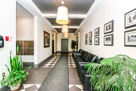 A hallway with a black and white checkered floor and a row of black leather chairs on the right side.