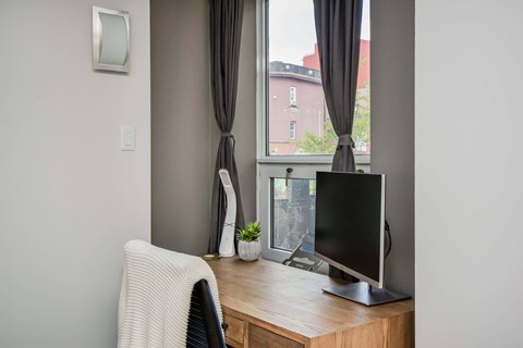 A black computer monitor sits on a desk with a white chair and a small potted plant.
