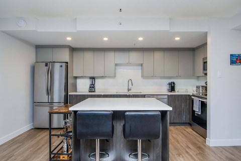 A modern kitchen with a white island and black bar stools.