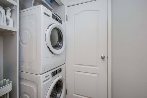 A white washing machine is stacked on top of another in a small laundry room.
