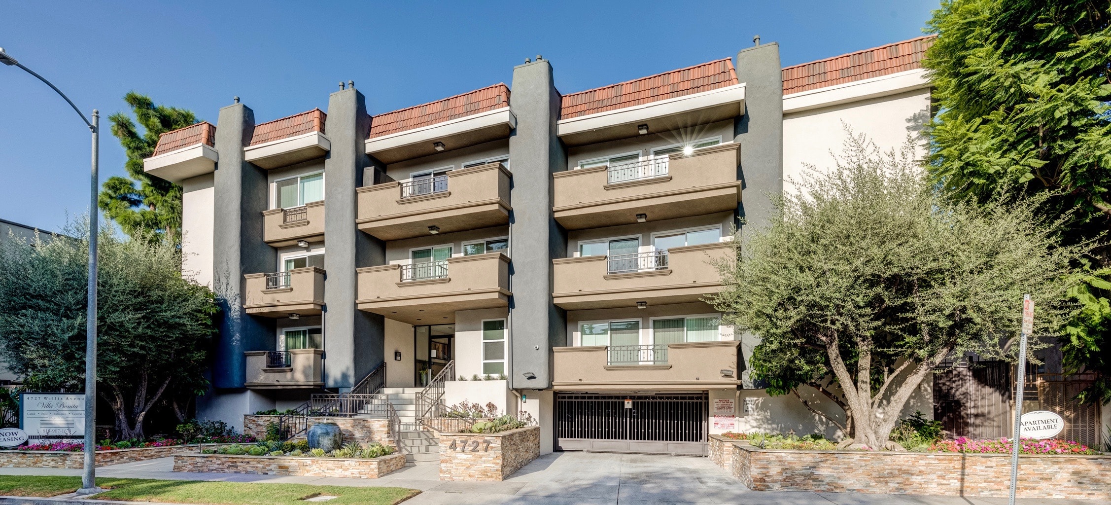 A large apartment building with a garage door and a tree in front.