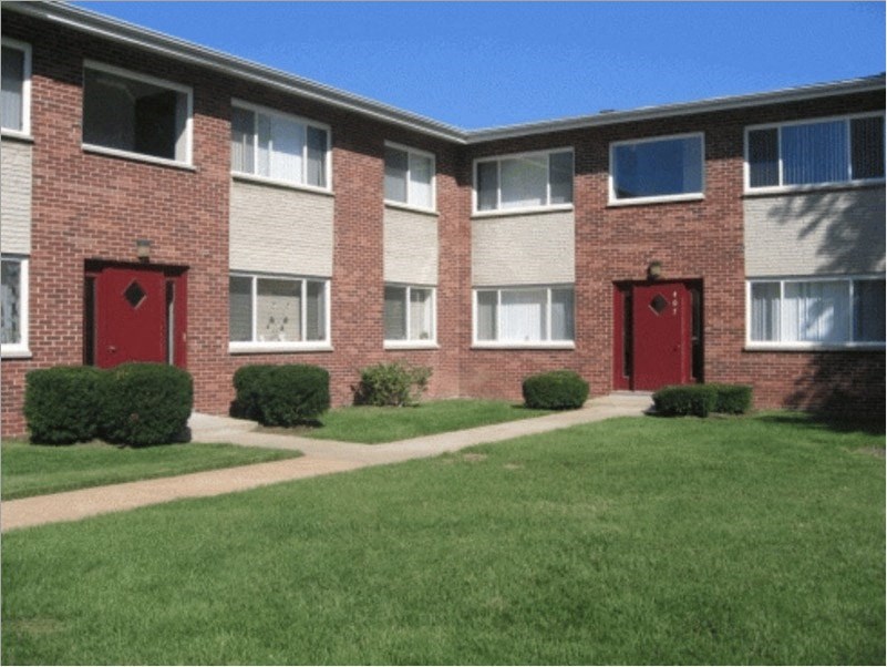 a brick apartment building with red doors and green grass