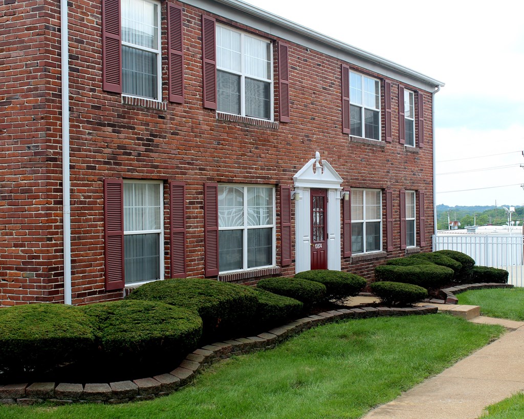 the front of a brick building with a red door and windows