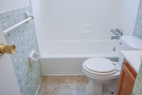 A white toilet sits in a bathroom next to a white bathtub.