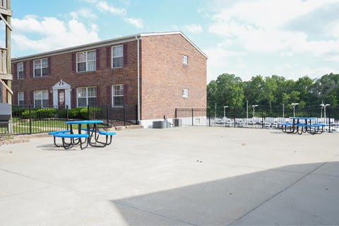 A red brick building with a white door and windows, a black fence, and a blue picnic table.