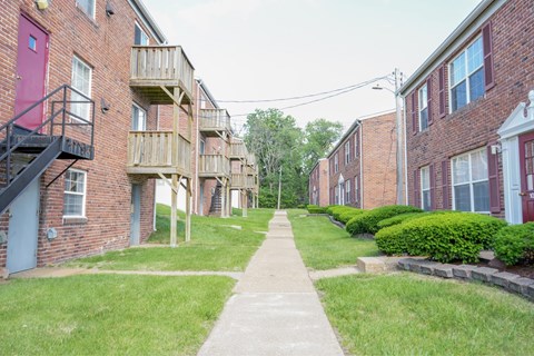 A long concrete walkway leads between two rows of red brick apartment buildings.