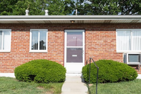 A red brick house with a purple door and two green bushes.