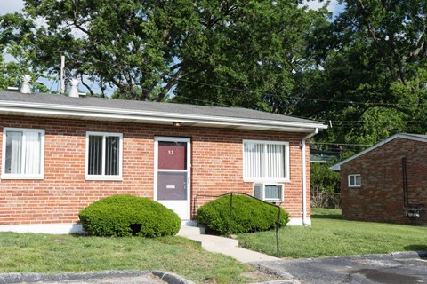 A red brick house with a black fence and green bushes.