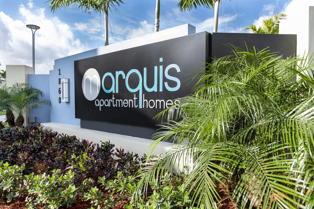 a sign for an acquis investment home in front of palm trees
