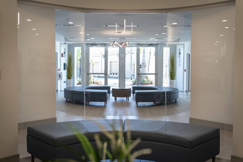 A spacious waiting area with a bench in the foreground and a view of a lounge area through the glass wall.