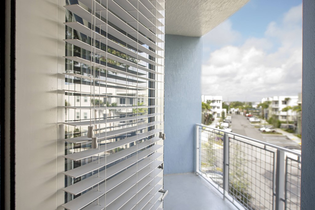 a balcony with white blinds and a view of a city