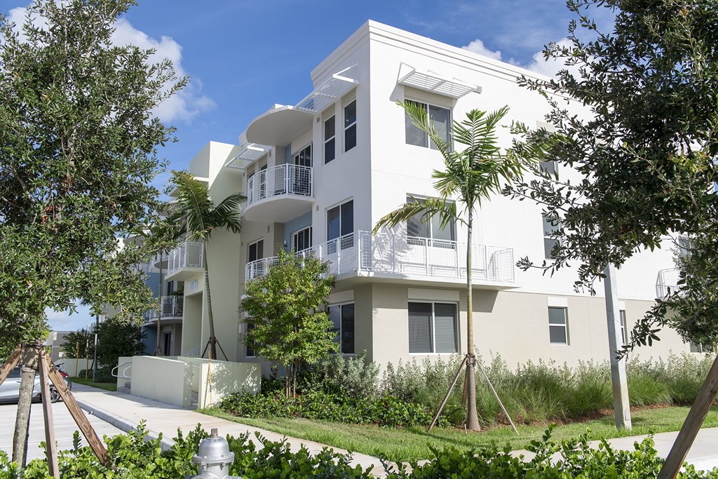 A white apartment building with balconies and trees in front.
