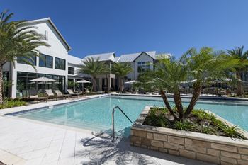 A pool surrounded by palm trees and a building in the background.