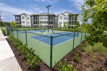 A tennis court is surrounded by a green fence and vegetation.