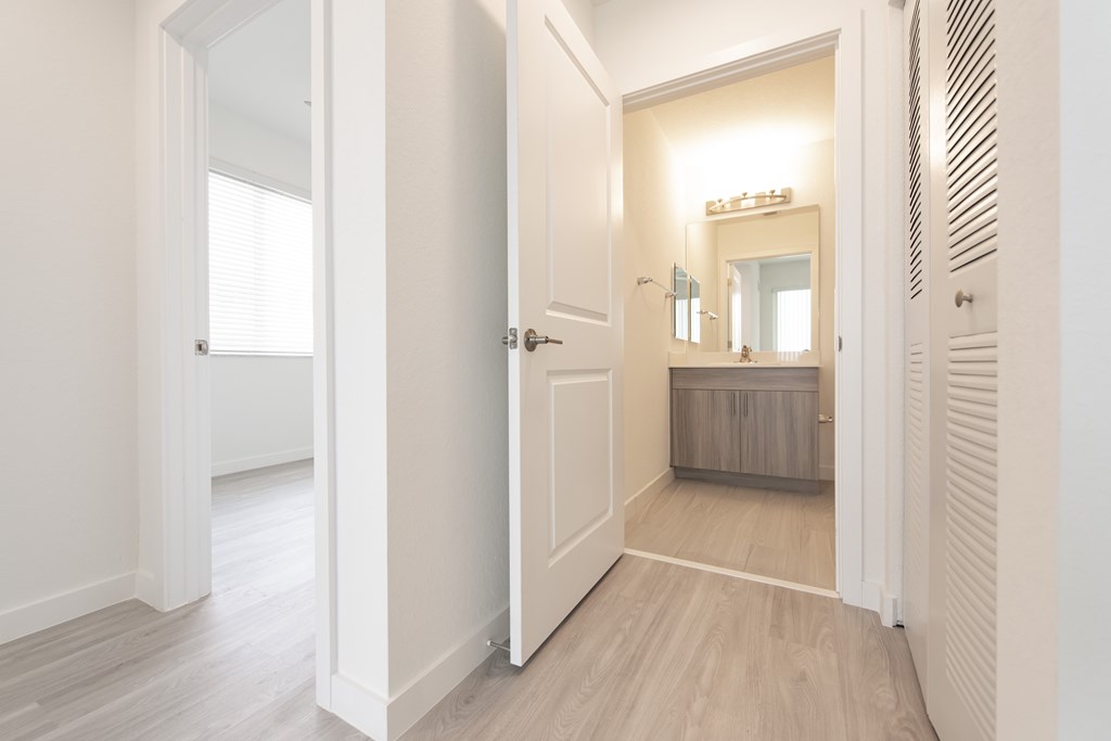 A white hallway with a mirrored doorway leading to a bedroom.