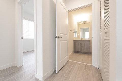 A white hallway with a mirrored doorway leading to a bedroom.