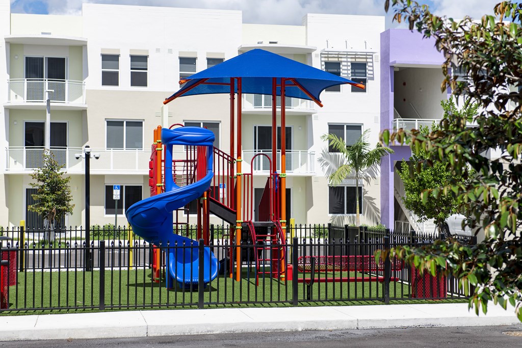 A playground with a blue slide and a red slide in front of a white building.