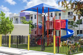 A playground with a red and blue slide and a purple and white building in the background.