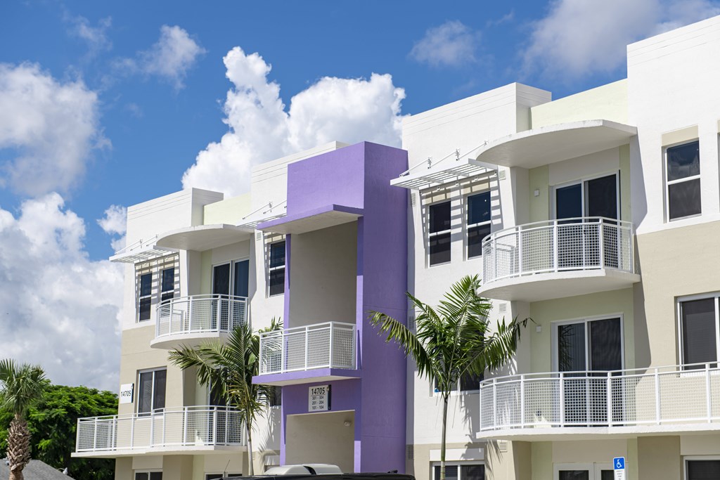 A white and purple building with balconies and palm trees in front.