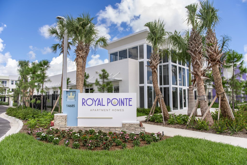 A sign for Royal Pointe Apartment Homes is in front of a building with a blue sky and palm trees in the background.