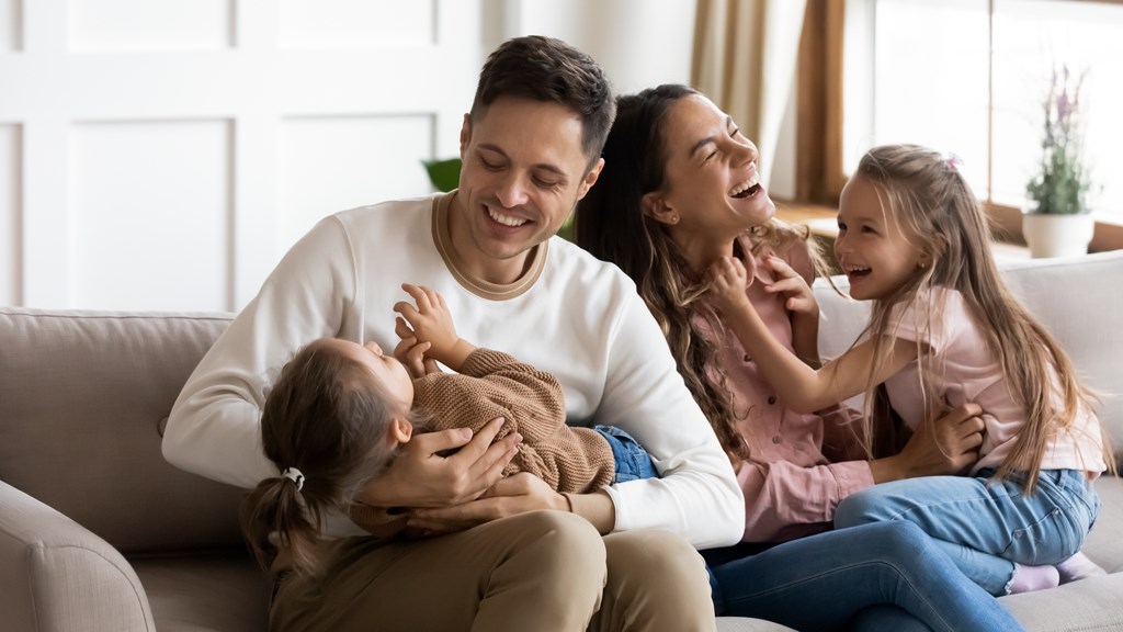 A family of four is sitting on a couch, sharing a joyful moment together.