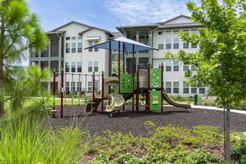 A playground with a green slide and red railings in front of a white building.