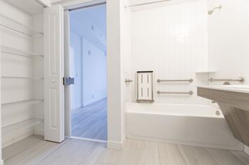 A white bathroom with a tub, sink, and a doorway leading to another room.