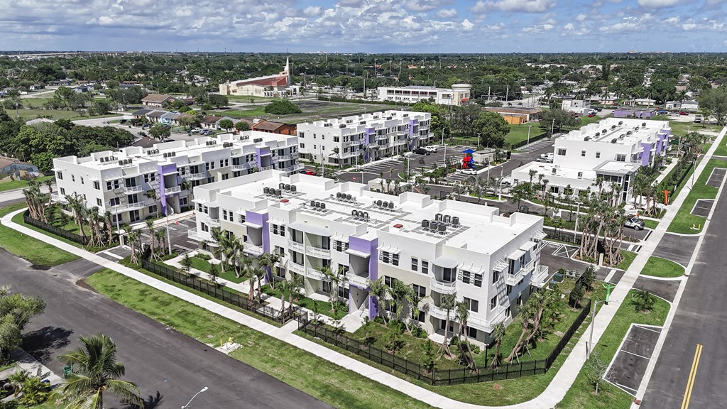 A large white building with a purple stripe on the side is surrounded by a green lawn and a black fence.