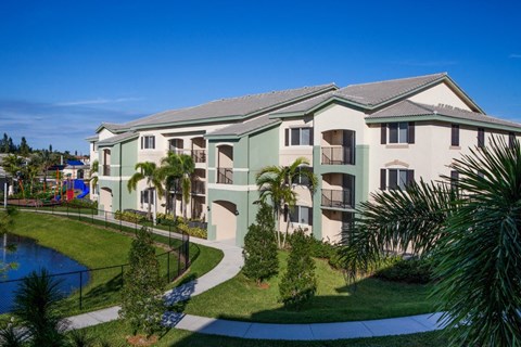 A building with a green roof and white walls with balconies and a pool in front.