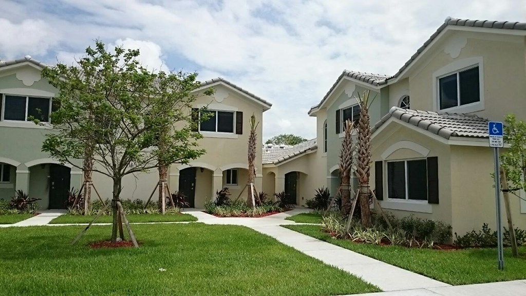 a group of white houses with grass and trees and a sidewalk