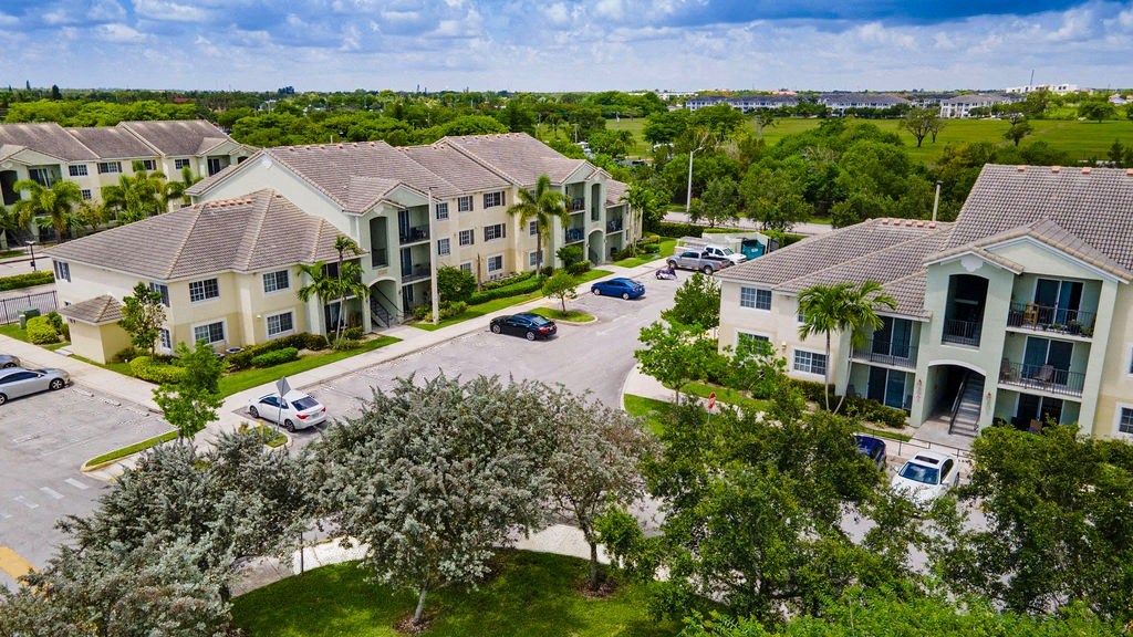 an aerial view of a group of apartment buildings with trees and cars parked in front