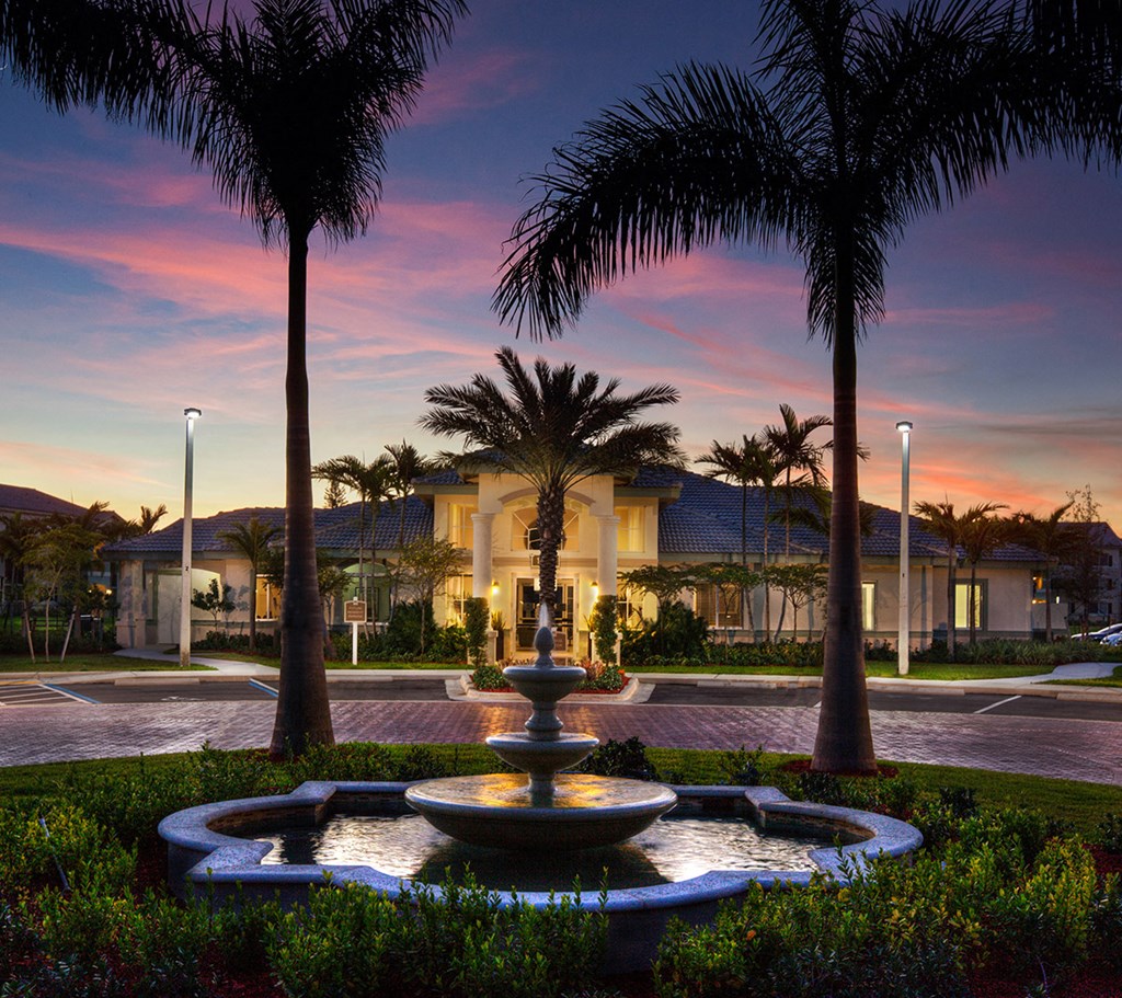 a fountain in a courtyard with palm trees at sunset