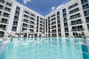 A large swimming pool in front of a white building with balconies.