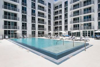 A large swimming pool in front of a building with lounge chairs and umbrellas.