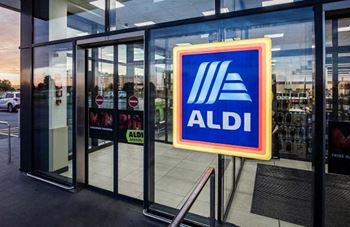 The image shows the entrance to an ALDI store with a large sign on the glass door.