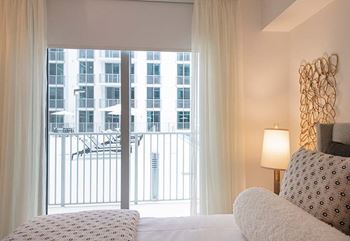 A bedroom with a large window overlooking a balcony with a view of a cityscape.