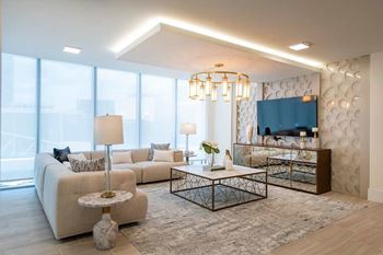 A modern living room with a white sofa, a glass coffee table, and a large window.