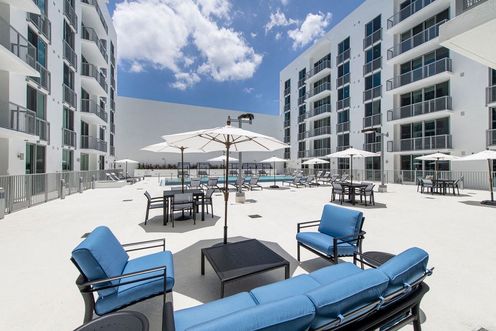 a patio with blue lounge chairs and umbrellas in front of a building