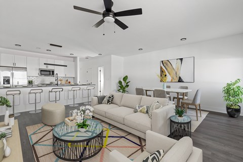 A modern living room with a white sofa set, a glass coffee table, and a ceiling fan.